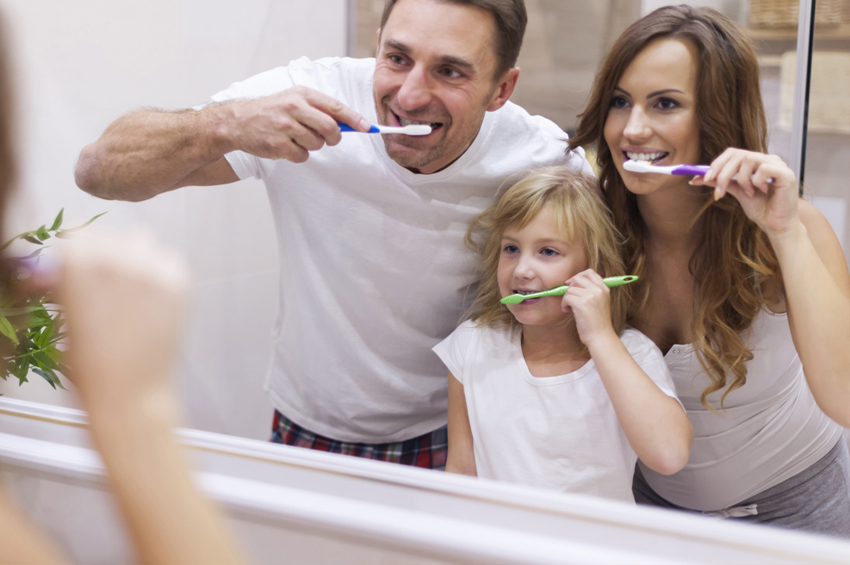 A family brushing their teeth in front of the mirror.